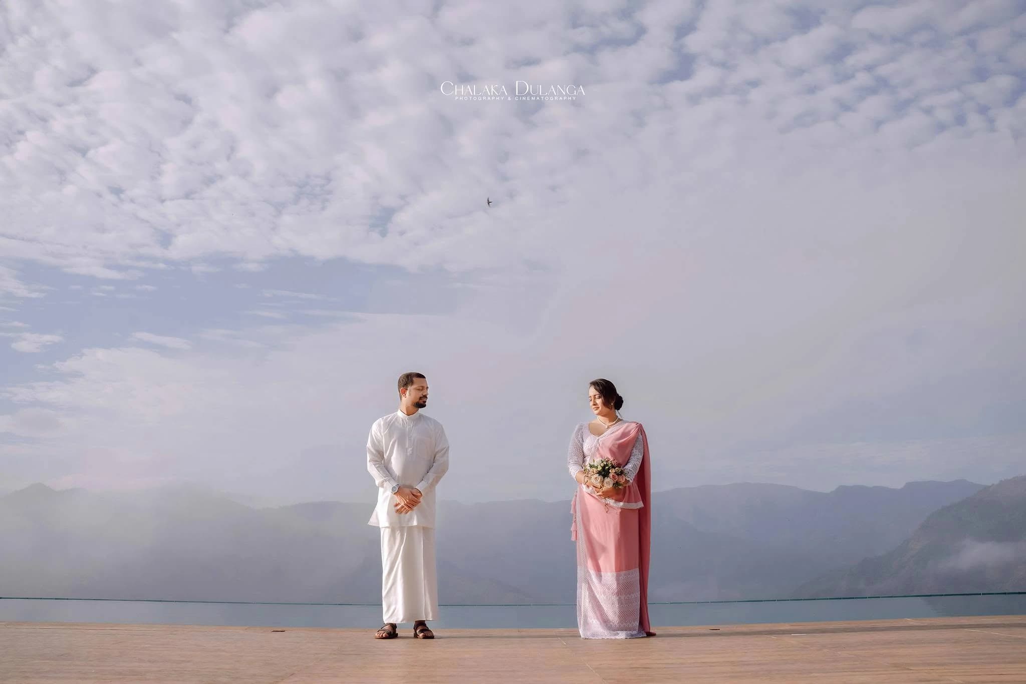 A couple in white and blush standing apart against a misty mountain sky