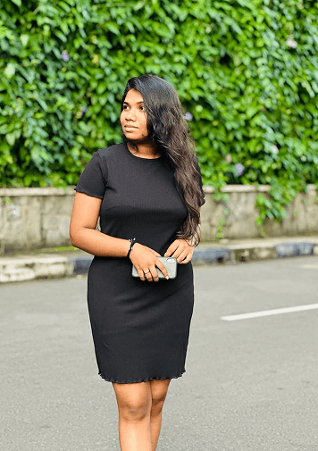 Duvini in a black dress standing in front of a leafy green wall