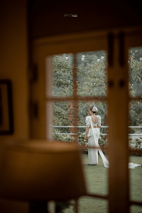 Bride seen through a window in a warmly lit, dark interior