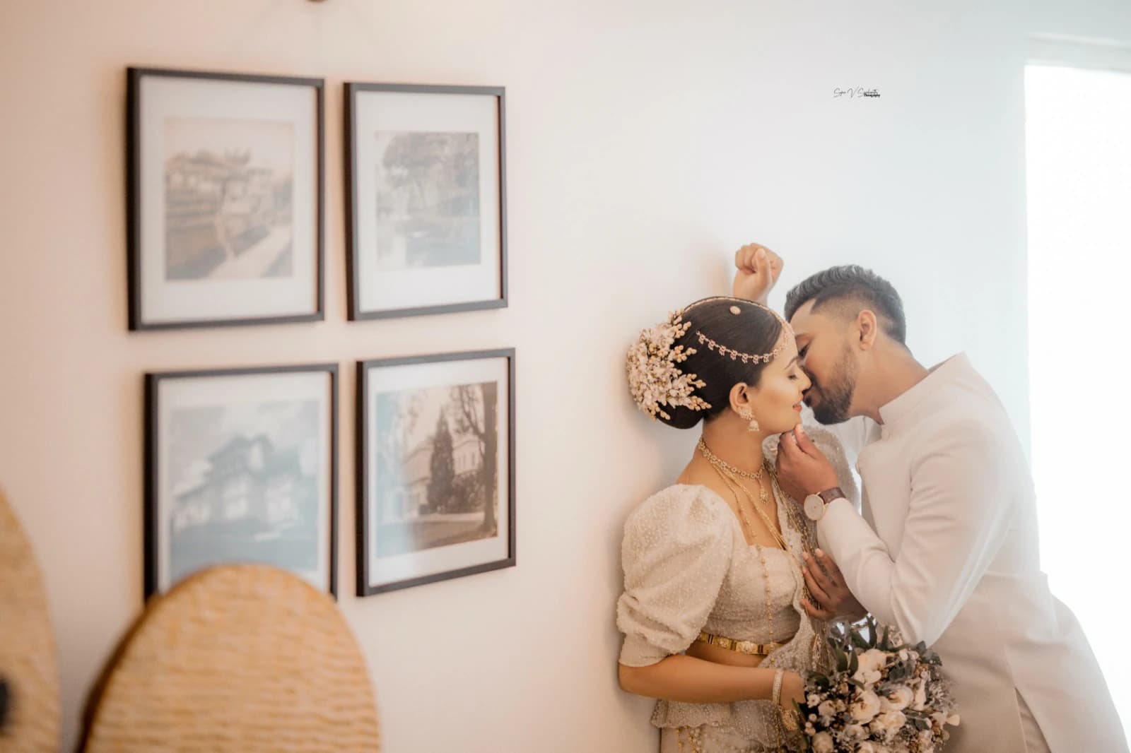A bride and groom embracing beside a wall of framed prints